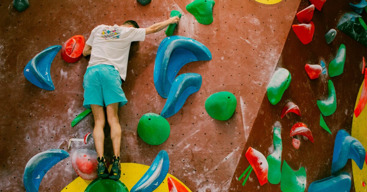 青と緑のホールドで壁を登る男性クライマーの後ろ姿