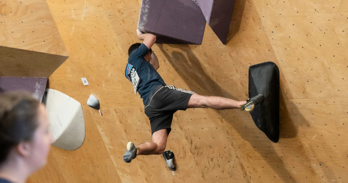 木製パネルのボルダリングウォールで登る男性クライマー