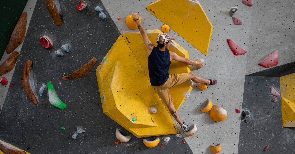 黄色いホールドが目立つクライミングウォールを登る男性クライマー