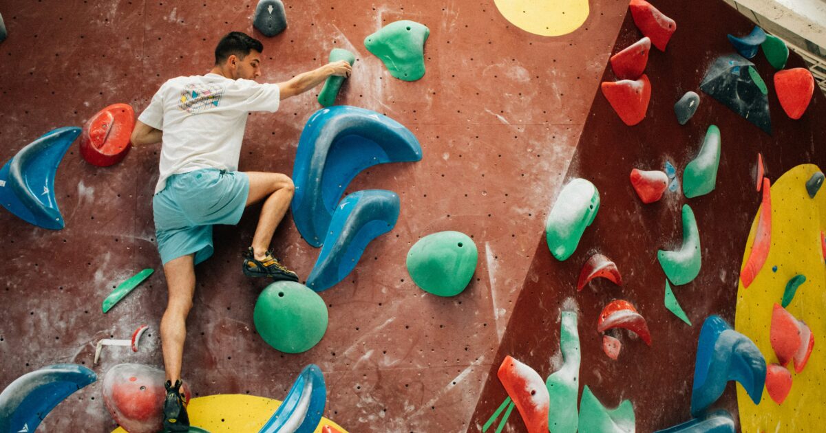 カラフルなホールドが配置されたボルダリングウォールを登る男性クライマー