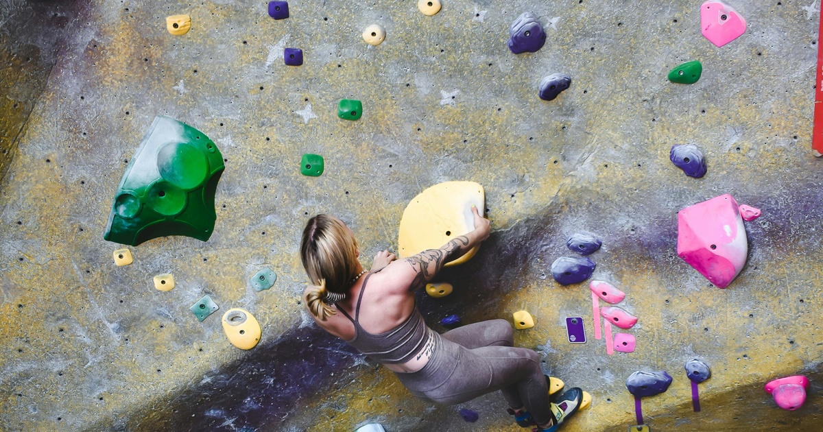 カラフルなホールドが配置された壁を登る女性クライマー