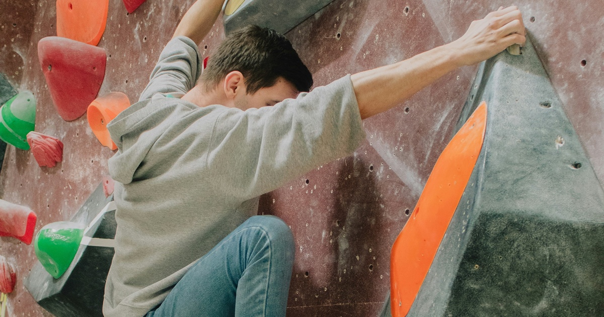 灰色とオレンジのホールドにしがみつく男性クライマー